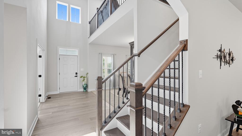 Two-story foyer with tall windows and a staircase with dark metal balusters and wood handrails.