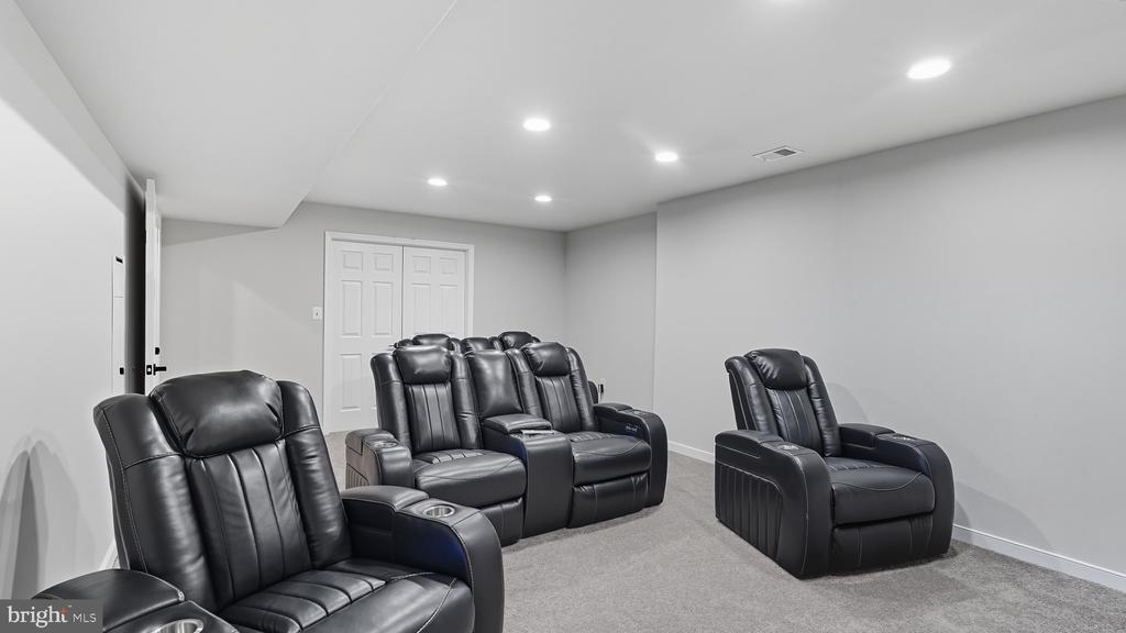 Home theater with black leather reclining seats, gray carpet, and recessed lighting.