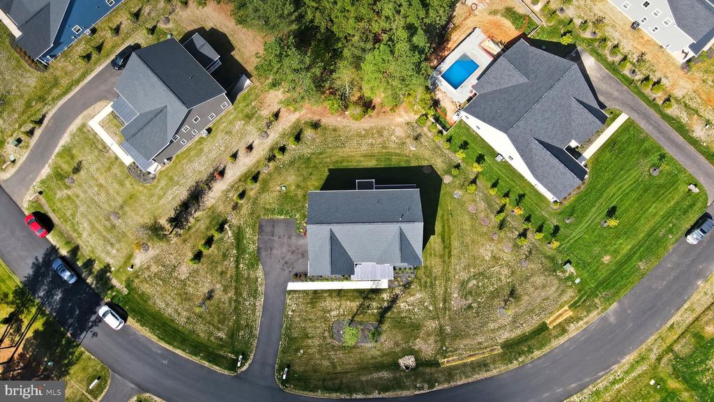 Aerial view of a detached house and its lot, with a driveway, lawn, and neighboring homes.