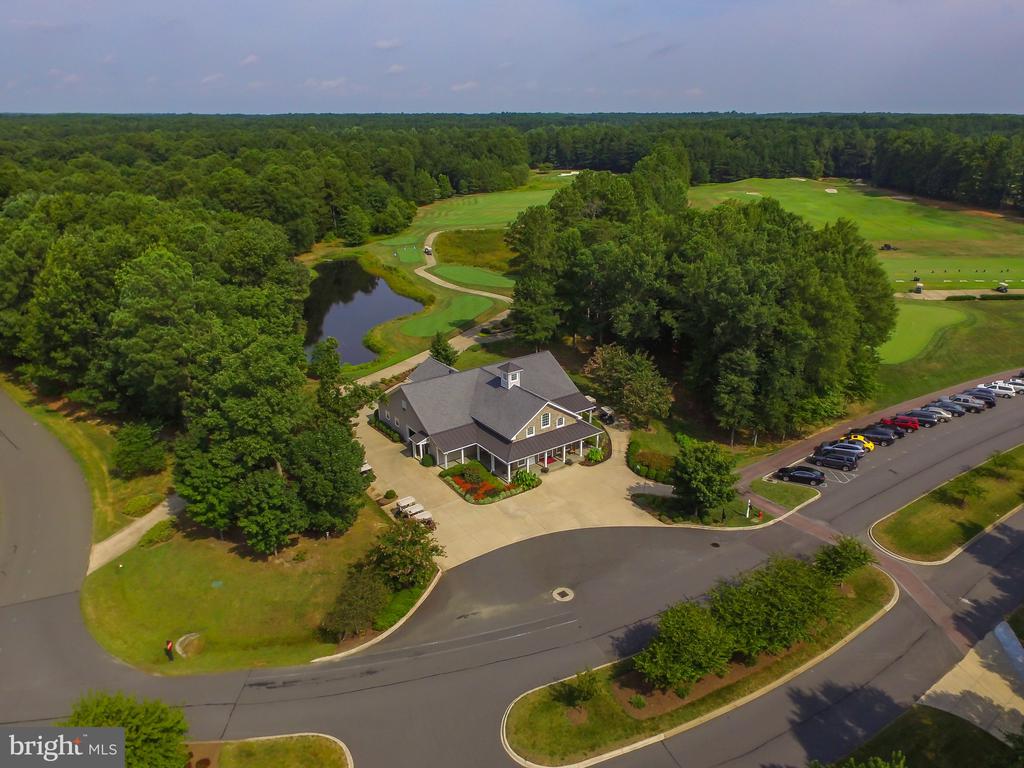 Aerial view of a clubhouse beside a golf course and pond, surrounded by trees.