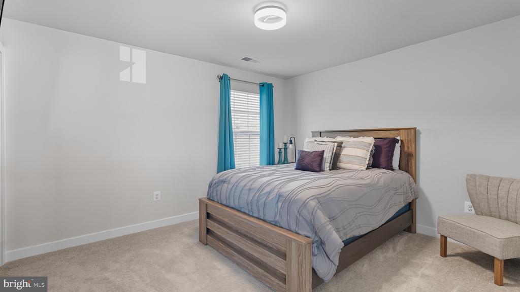 Furnished bedroom with a wooden bed, striped gray bedding, turquoise curtains, and a beige accent chair.