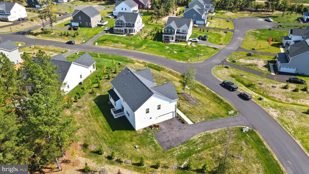 Aerial view of a white detached home with a dark roof and paved driveway.