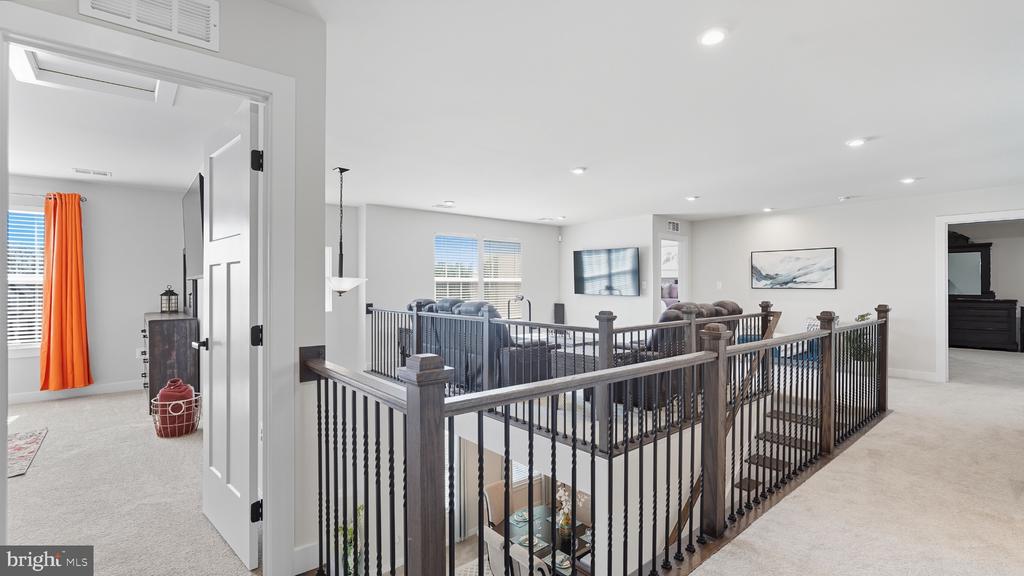 Upstairs landing with dark railings overlooking a furnished living room and open staircase.