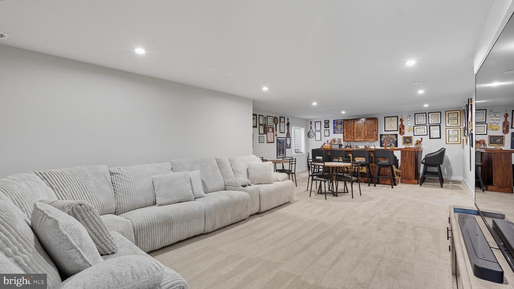 Basement living area with a long gray sectional, dining table, and wall of framed memorabilia.