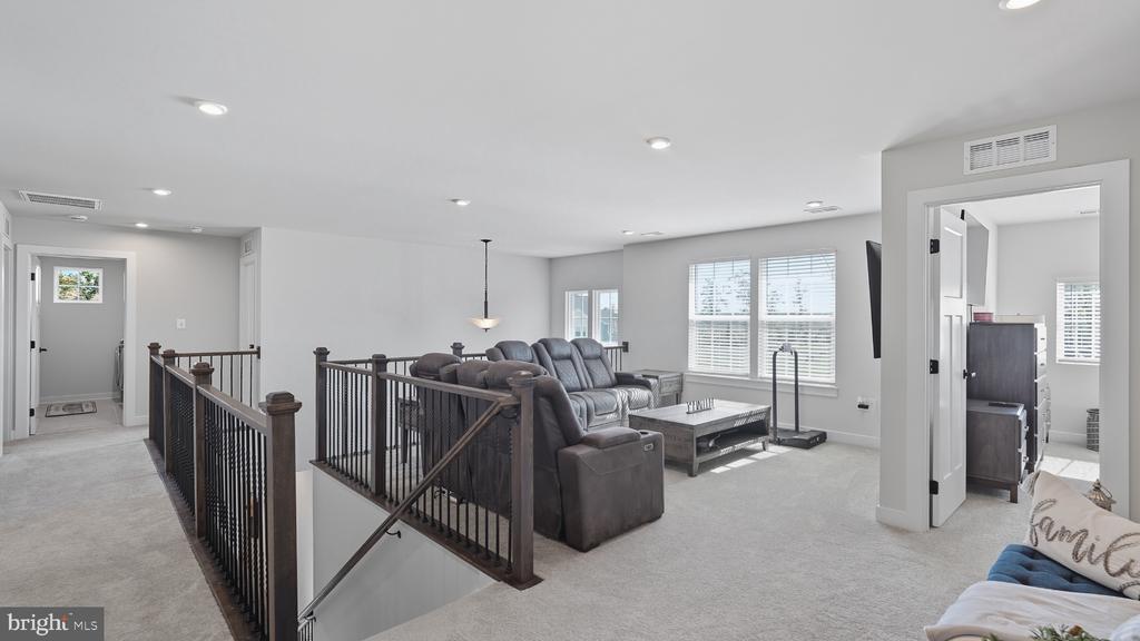 Upstairs living area with gray sectional, large windows, and dark railings surrounding an open stairwell.