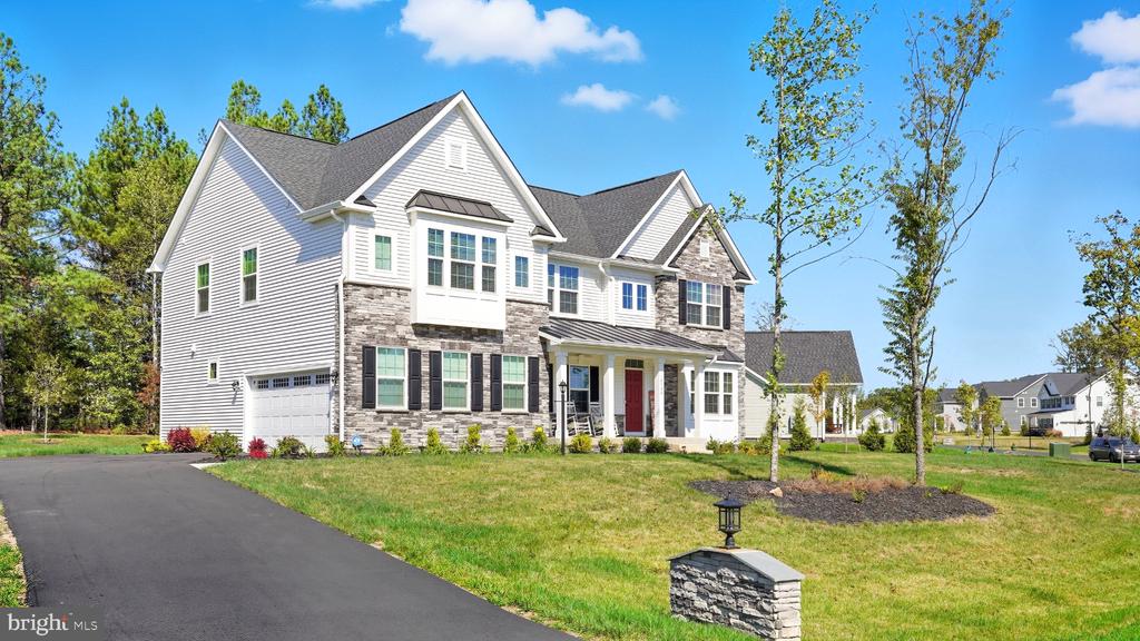 Two-story white house with stone accents, dark shutters, front porch, and curved driveway.