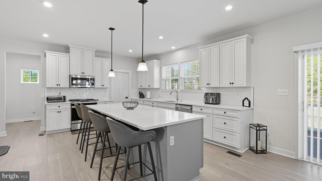 Bright kitchen with white cabinetry, a large island with bar seating, and stainless steel appliances.
