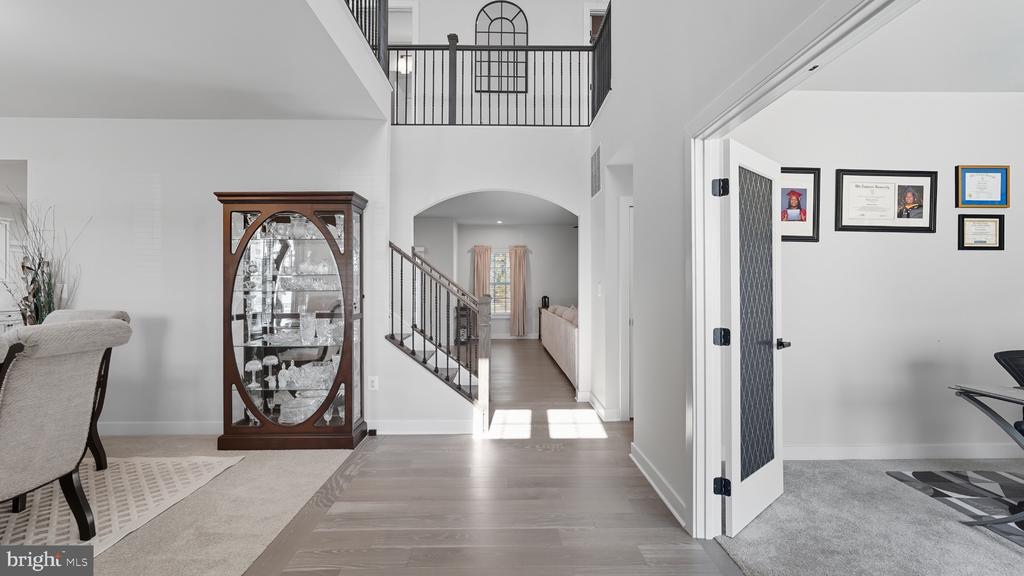 Two-story entryway with a glass-front display cabinet, black-railed staircase, and open carpeted room.