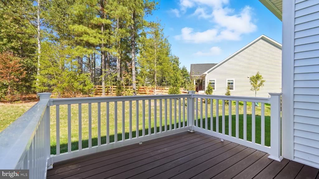 Raised deck with white railings overlooking a grassy backyard bordered by trees and a wooden fence.