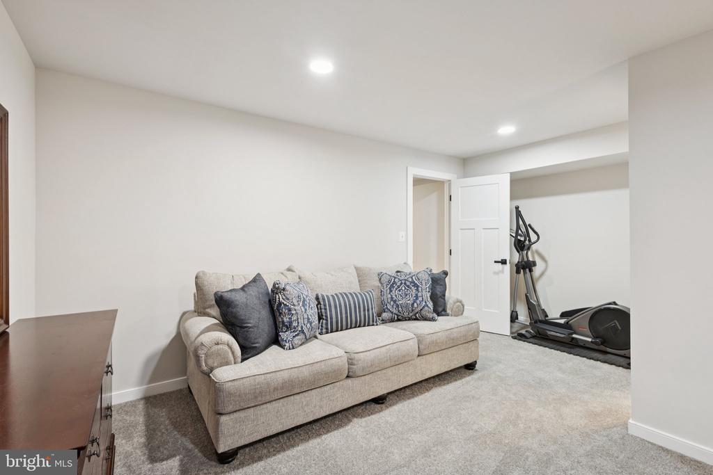 Basement sitting area with a beige sofa and an elliptical exercise machine beside the doorway.
