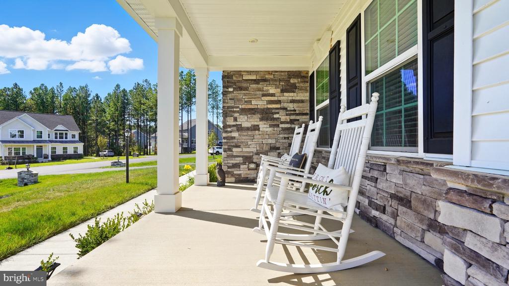 Front porch with white rocking chairs and a stone accent wall overlooking neighboring homes.