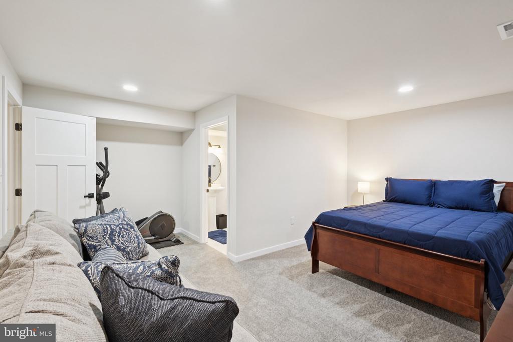 Basement bedroom with navy bedding, a sofa, and exercise equipment.
