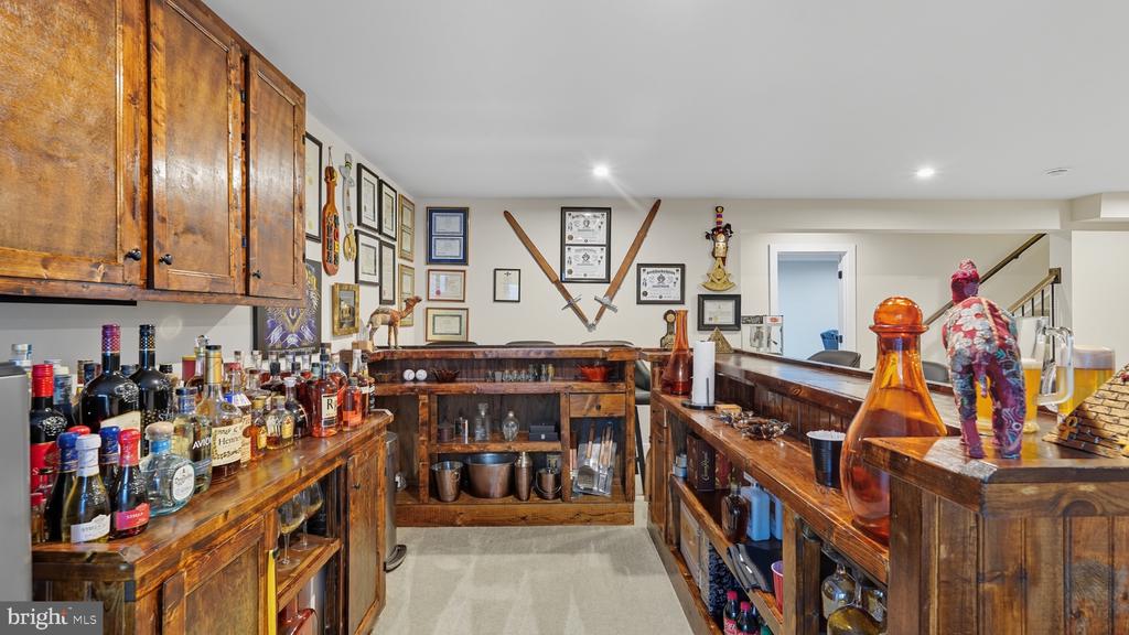 Home bar with dark wood cabinetry, liquor bottles, and crossed swords displayed on the wall.