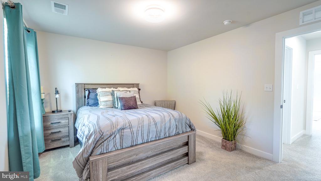 Furnished bedroom with a gray wood bed, striped bedding, teal curtains, and a potted plant.