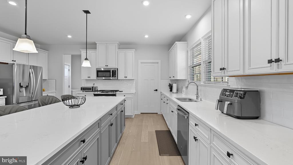 Modern white kitchen with a large island, stainless steel appliances, and light wood flooring.