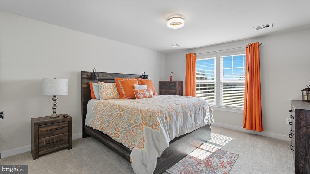 Bedroom with orange-accented bedding, dark wood furniture, and sunlit windows with orange curtains.