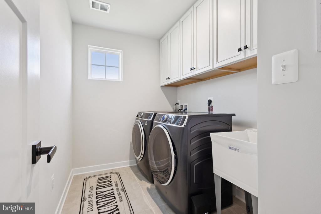 Laundry room with dark front-loading washer and dryer, white cabinets, and a utility sink.