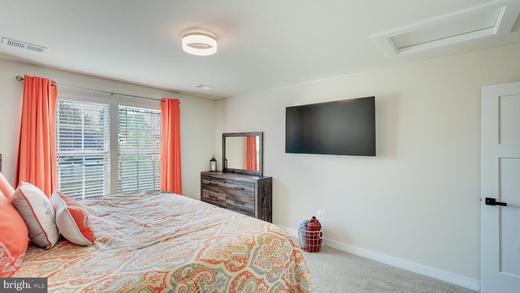 Furnished bedroom with a paisley bedspread, coral curtains, dresser, mirror, and wall-mounted television.