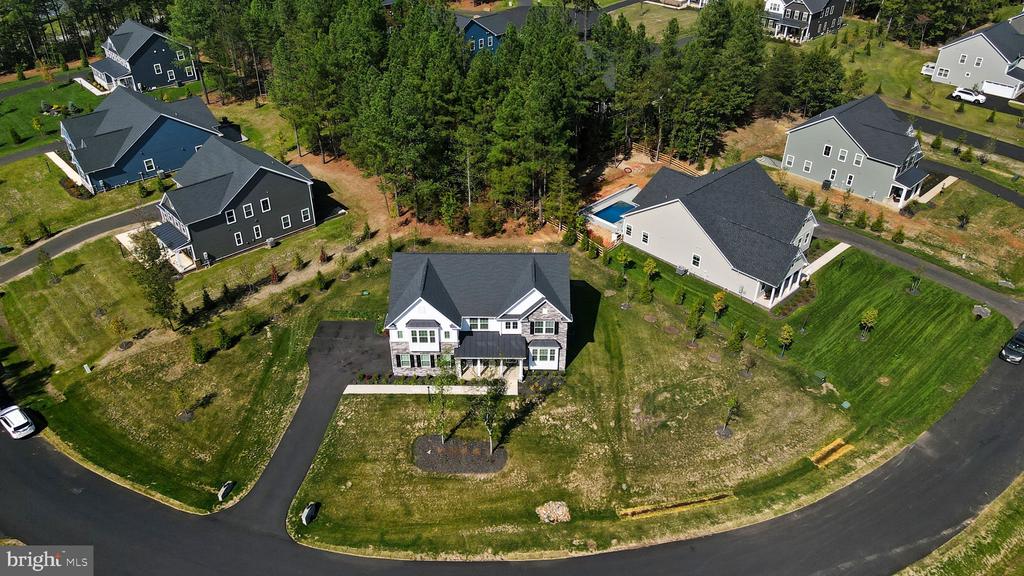 Aerial view of a detached house with a dark roof, front lawn, and neighboring homes along a curved street.