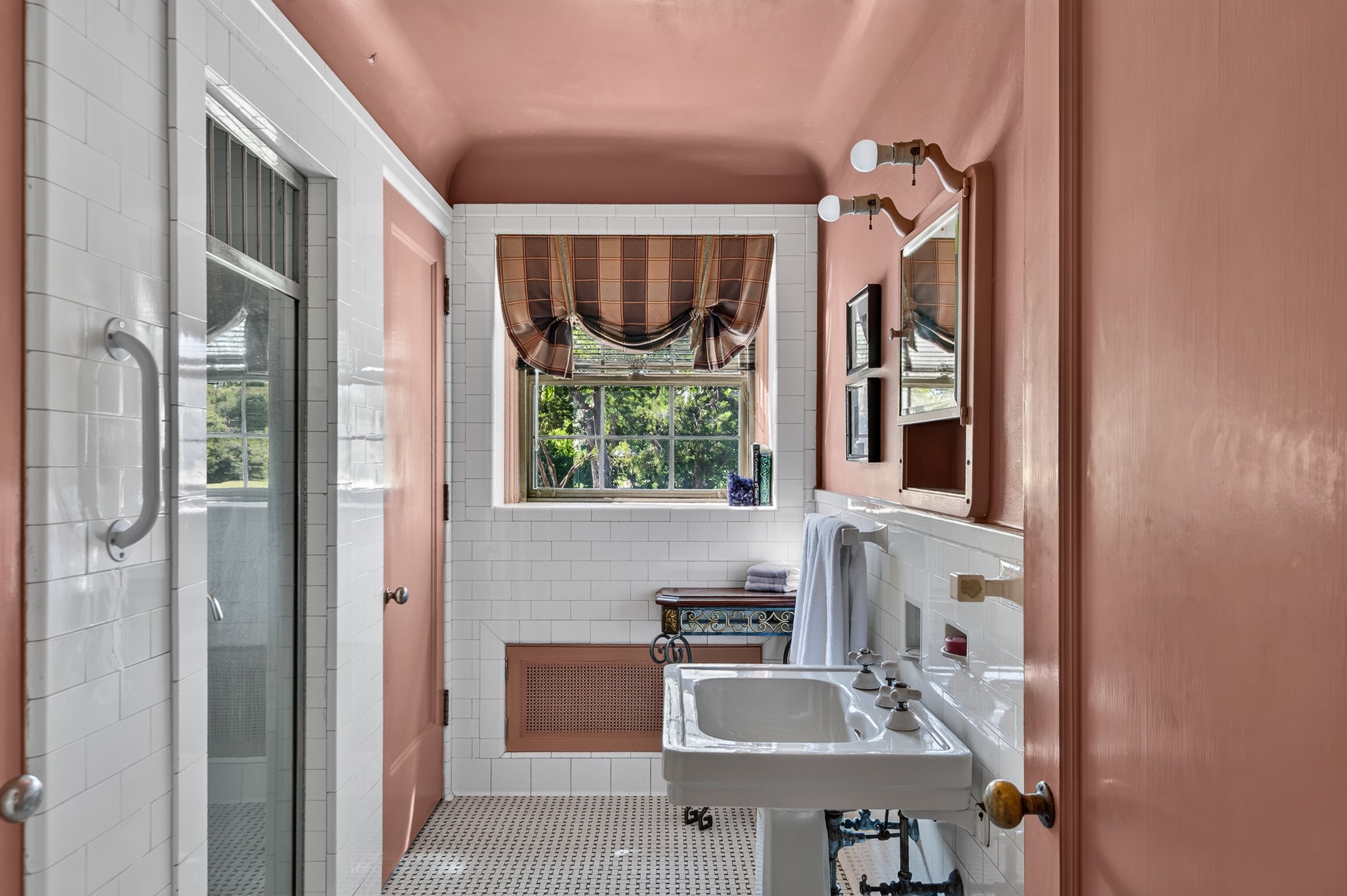 Bathroom with pink walls, white tile, a pedestal sink, and a window with a plaid valance.