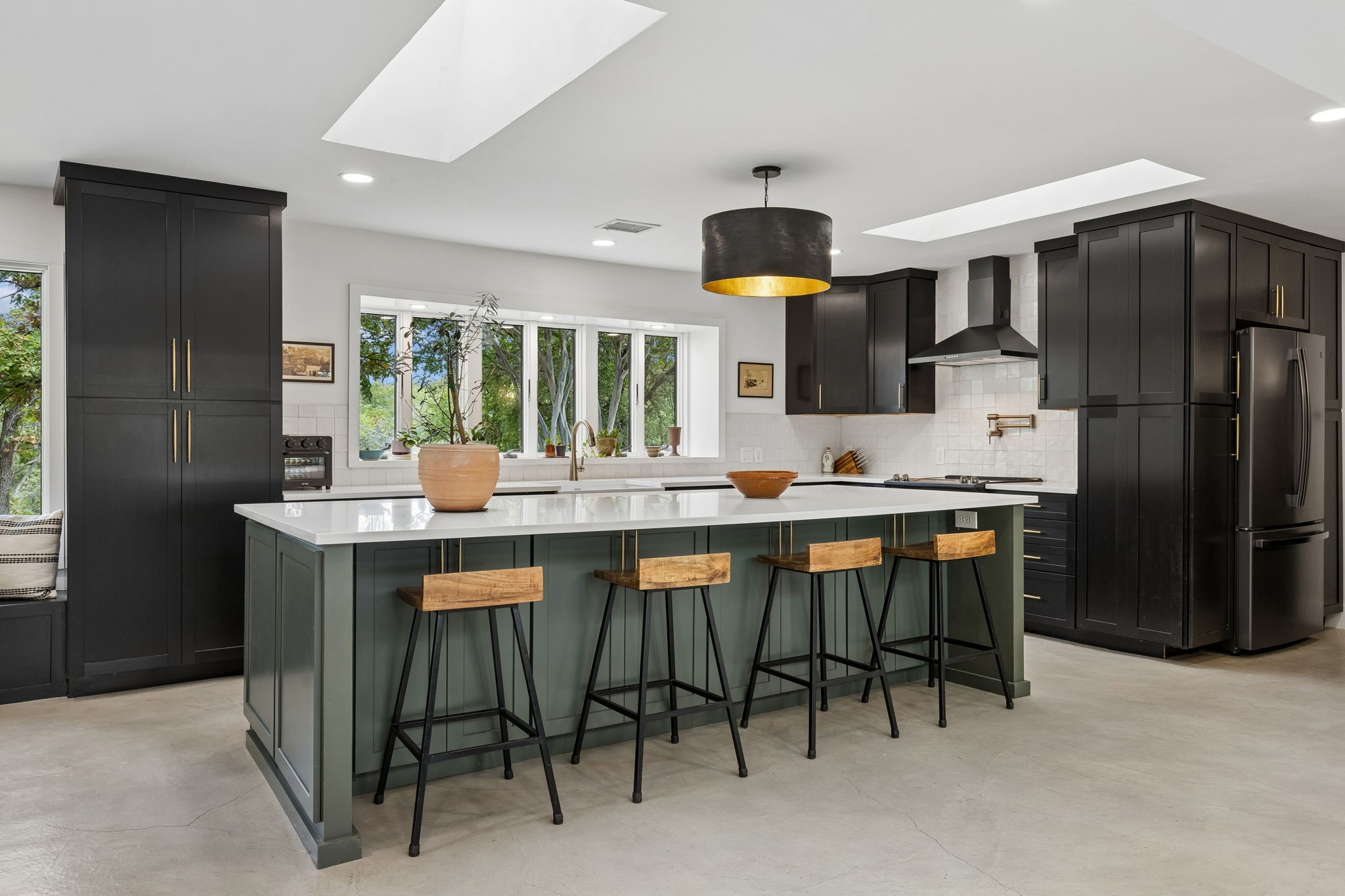 Modern kitchen with charcoal cabinets, a green island, white counters, and four wooden stools.