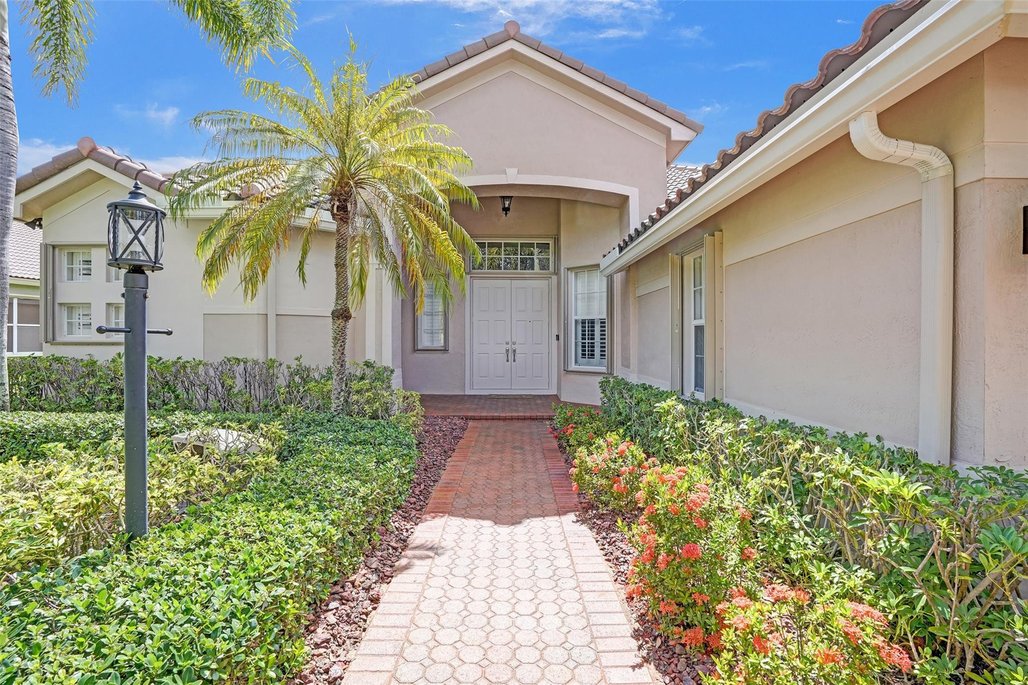 Home entrance with a paved walkway, tropical landscaping, and a palm tree.