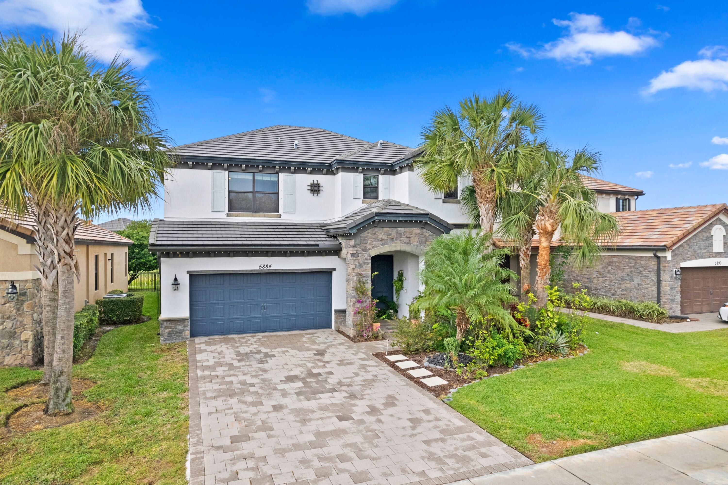 Two-story white home with a blue garage door, stone entry, palm trees, and paved driveway.