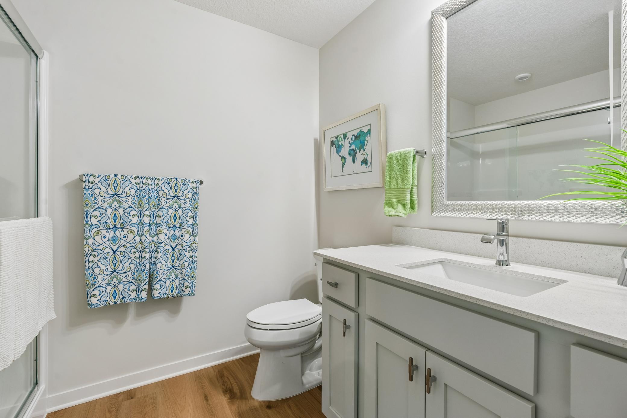 Bathroom with a pale gray vanity, large mirror, glass shower, and patterned towels.