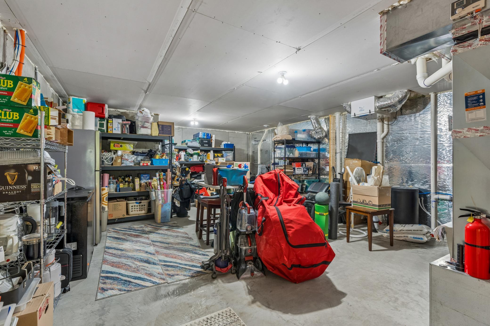 Basement storage area with crowded shelves, exposed insulation, utility equipment, and a large red-covered item.
