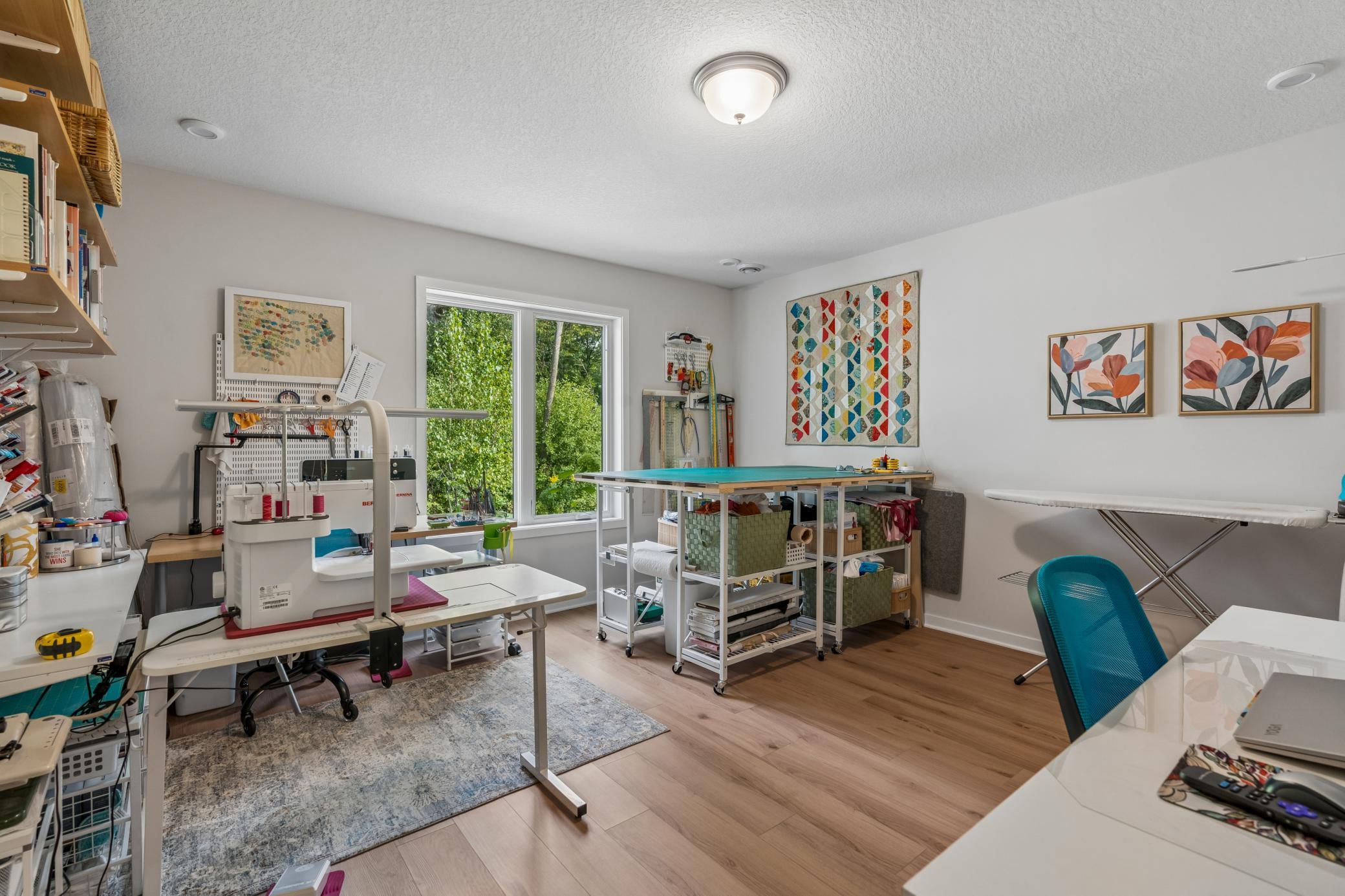 Craft room with sewing machines, organized supplies, and worktables beside large windows.