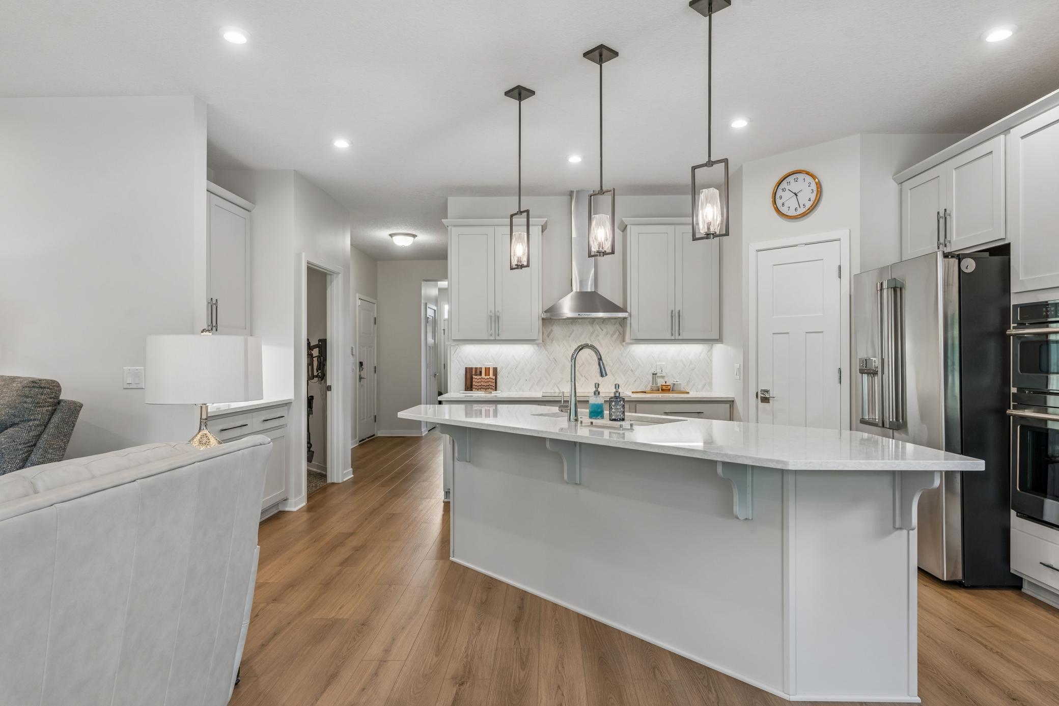 Bright white kitchen with a large island, stainless steel appliances, and warm wood flooring.