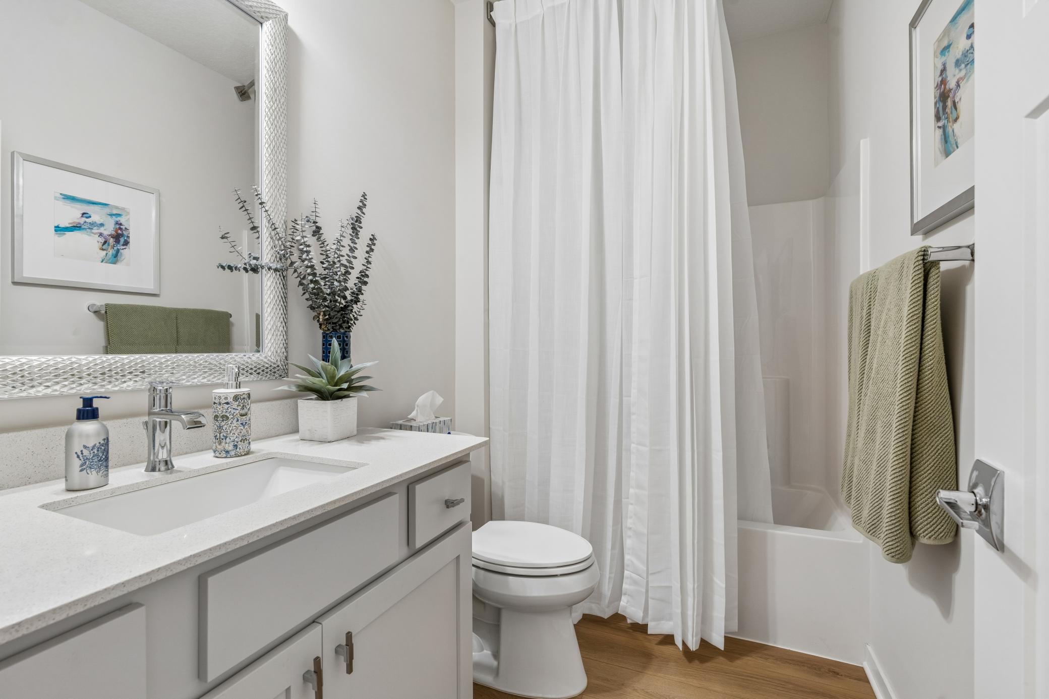 Bright bathroom with a white vanity, silver-framed mirror, and tub behind a shower curtain.