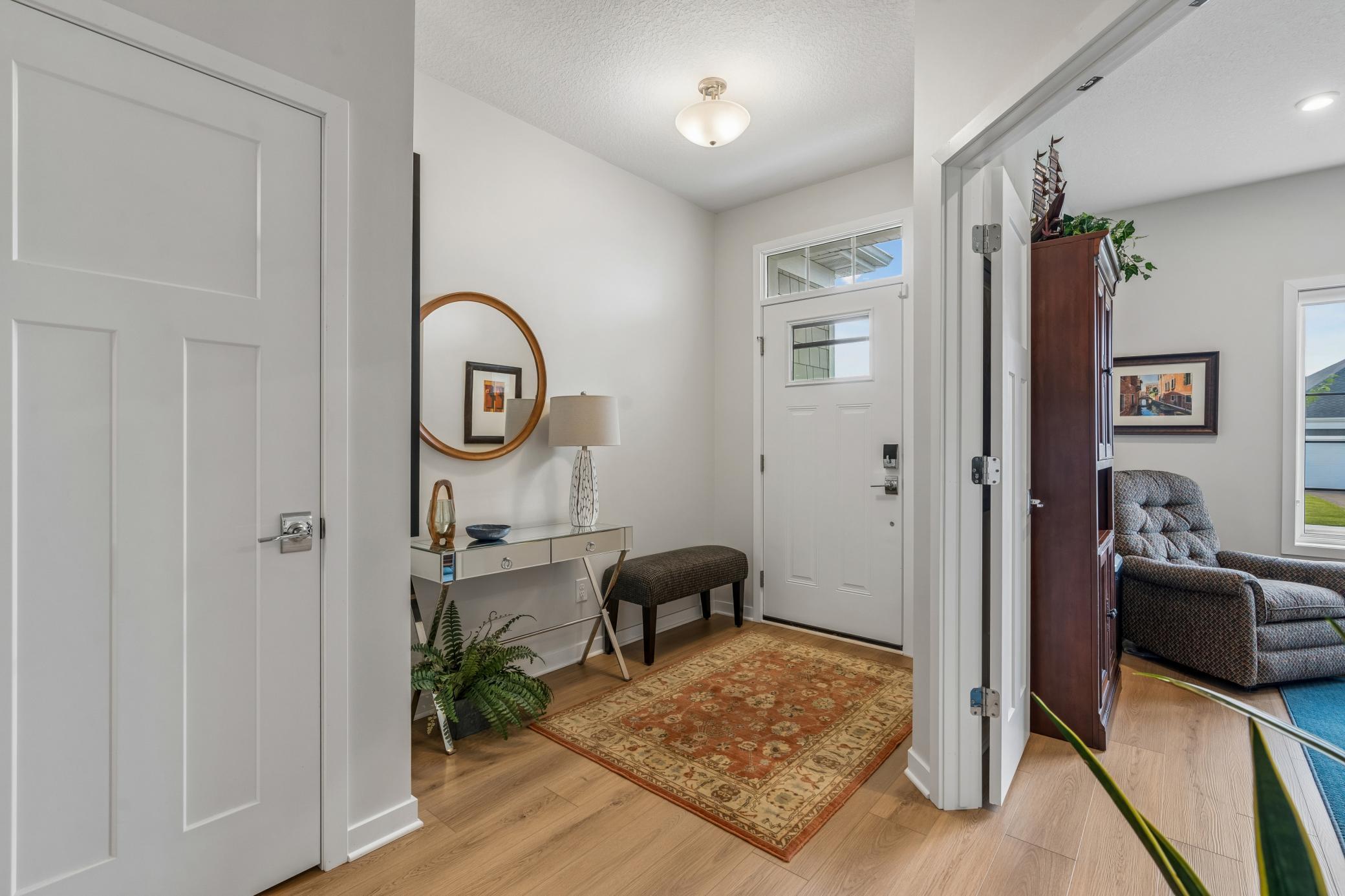Furnished entryway with a patterned rug, console table, round mirror, and view into the living room.
