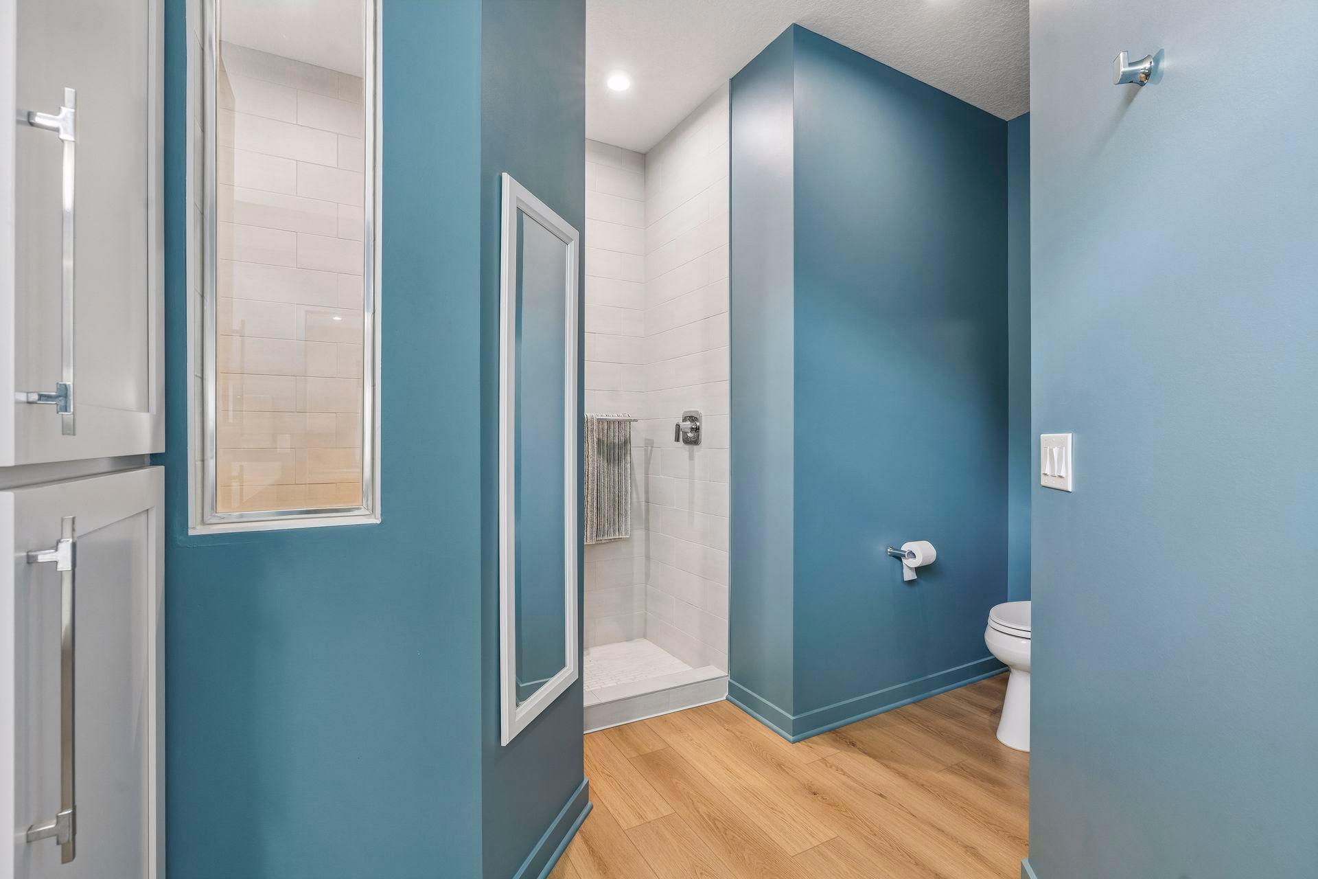 Bathroom with a white-tiled walk-in shower, teal walls, and wood-look flooring.