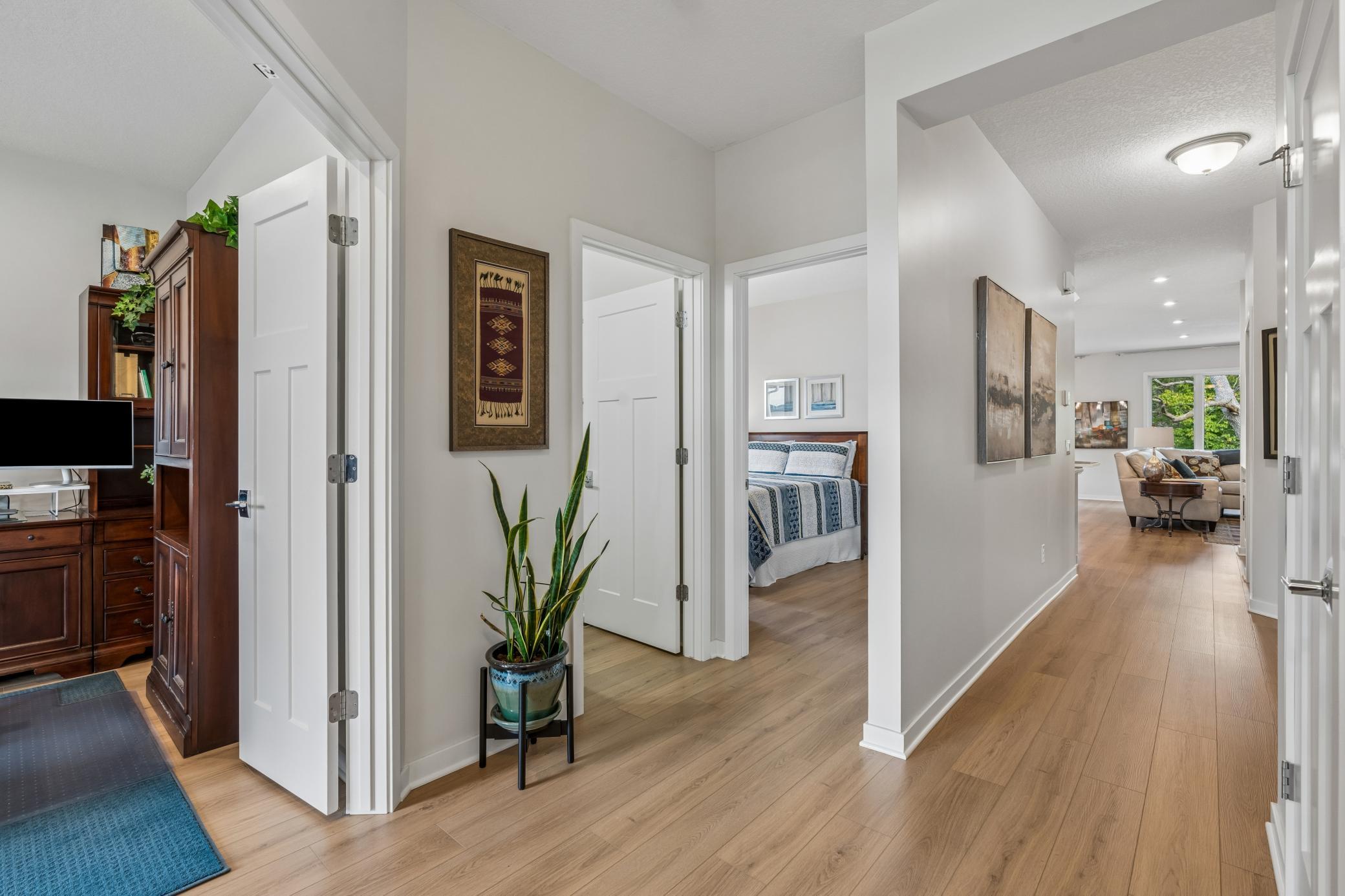 Wood-floored hallway with a potted snake plant and open doorways to furnished rooms.