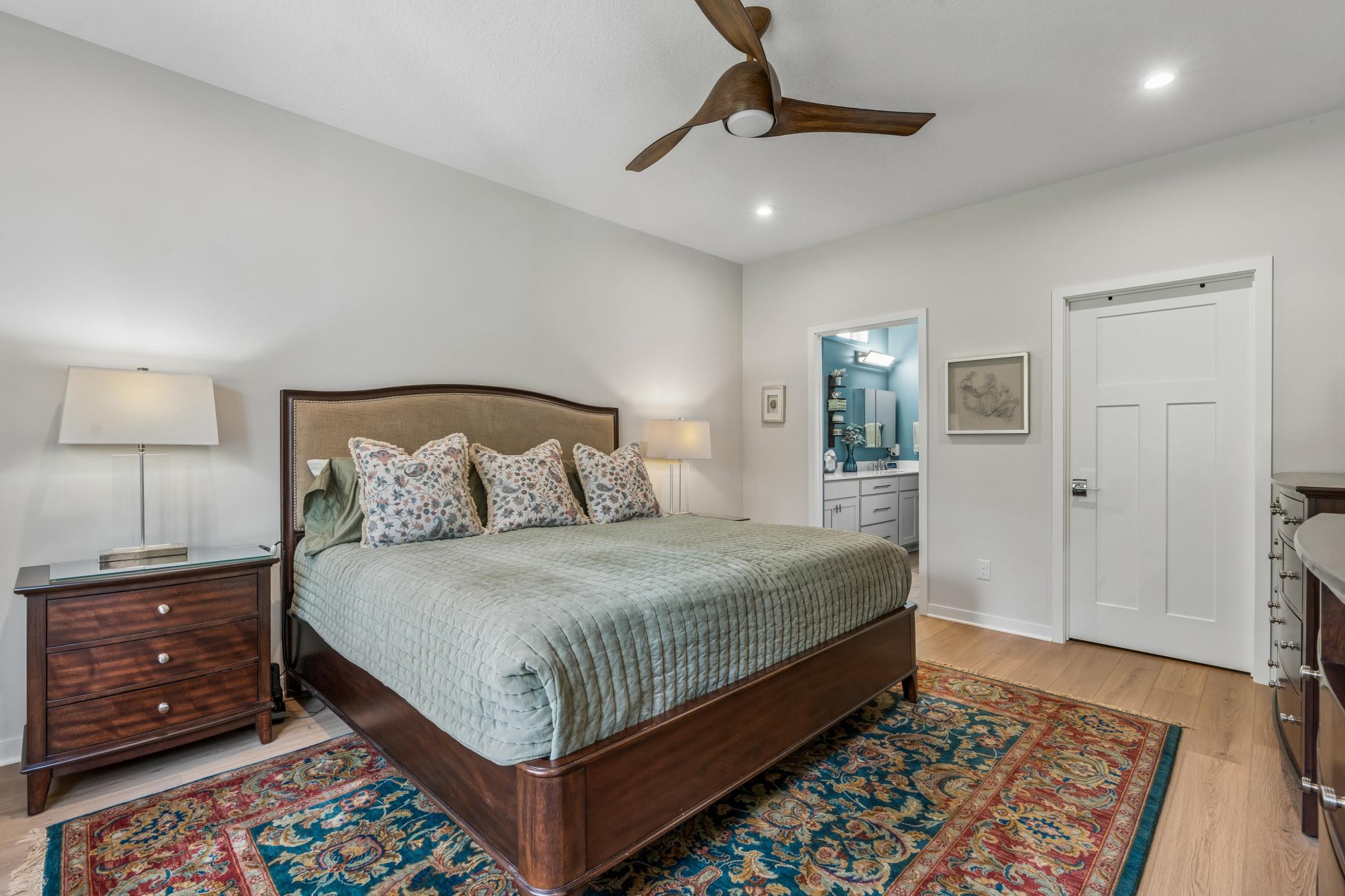 Furnished bedroom with a dark wood bed, pale green quilt, and doorway to a blue bathroom.