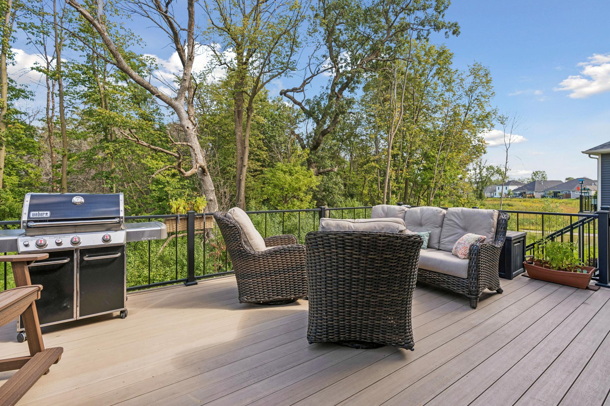 Furnished deck with a gas grill and wicker seating overlooking mature trees.