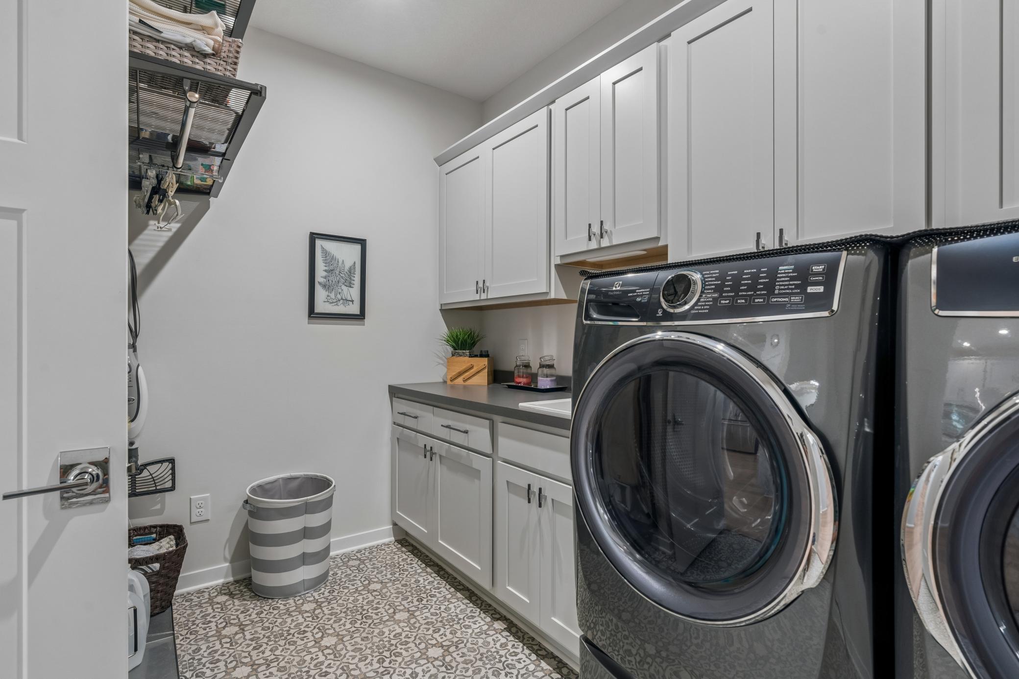 Laundry room with front-loading machines, white cabinets, and patterned tile flooring.