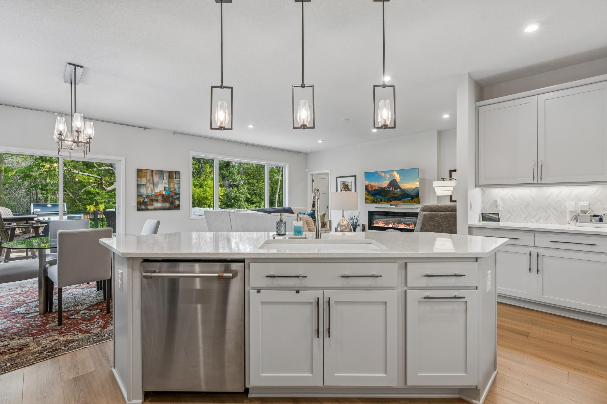 Bright kitchen with a large white island, stainless dishwasher, and windows overlooking trees.