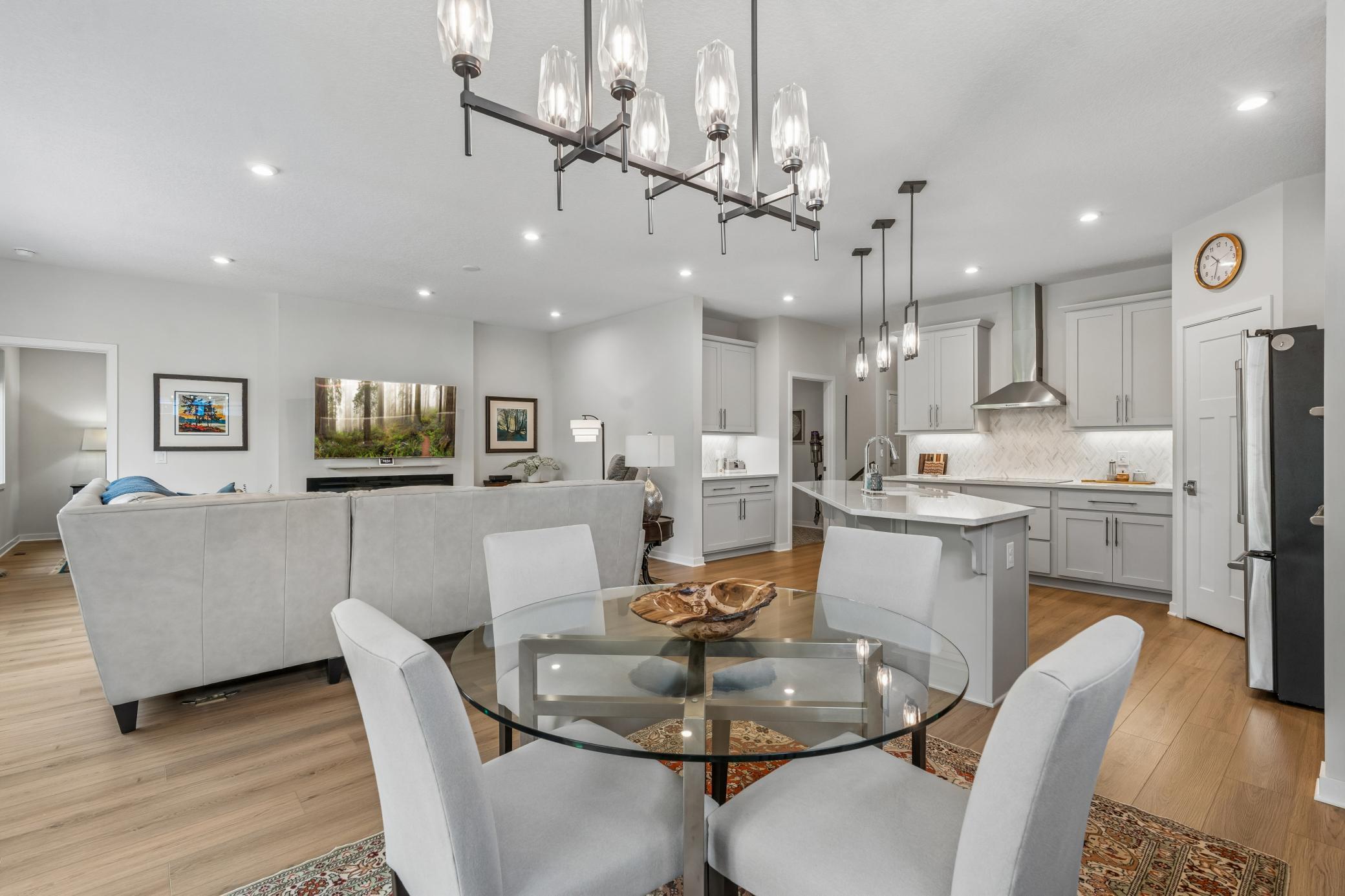 Open-concept kitchen and living area with gray cabinetry, a white island, and a round glass dining table.