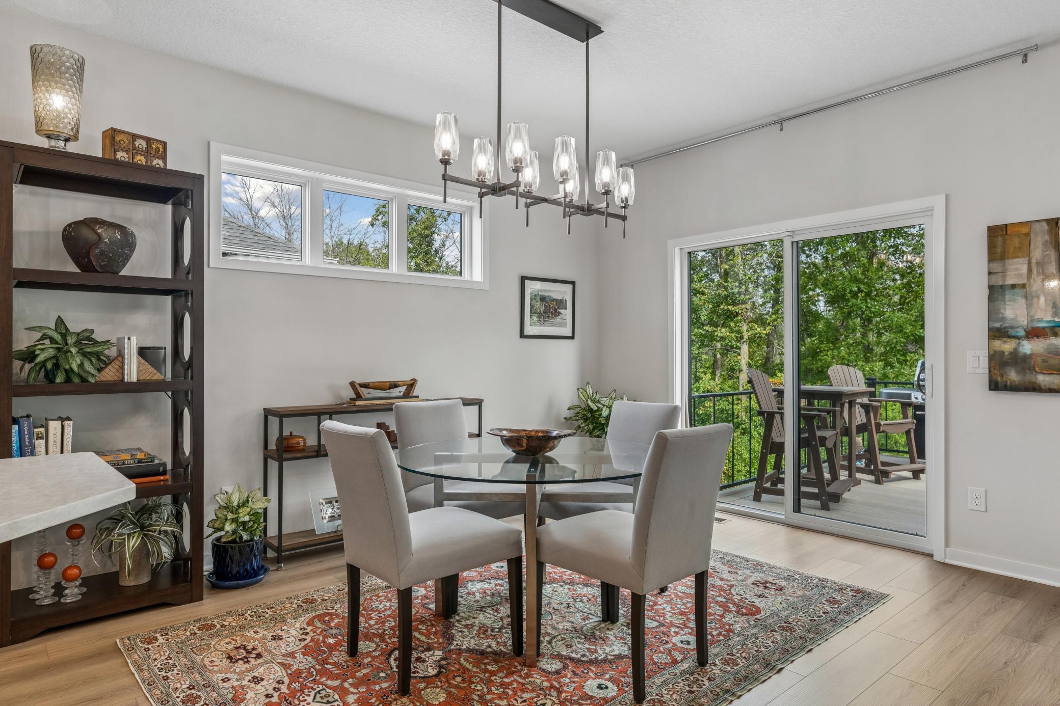 Staged dining room with a glass-top table, patterned rug, and sliding doors to a tree-lined deck.