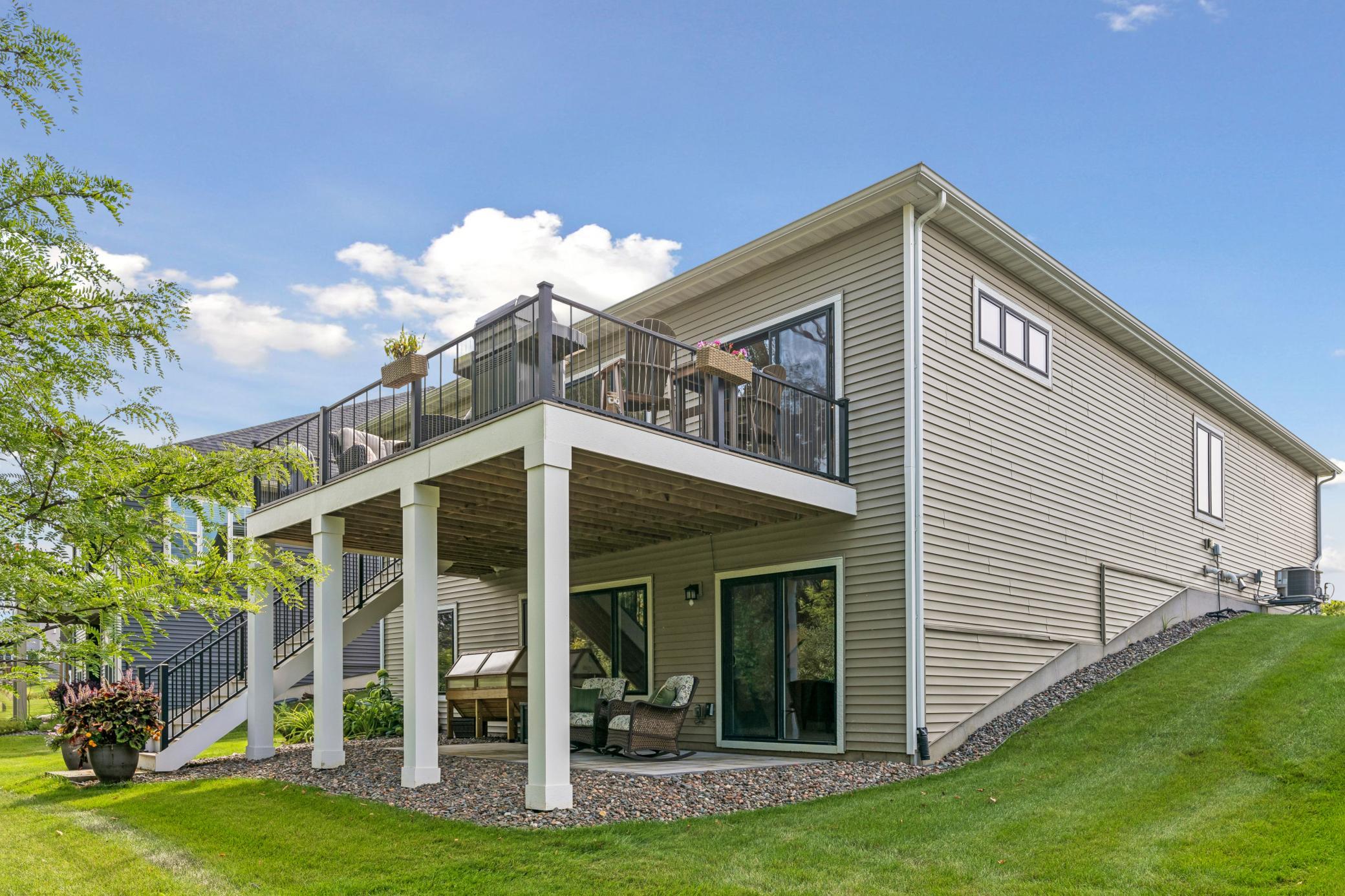 Home’s rear deck with black railings and stairs above a shaded patio with seating.
