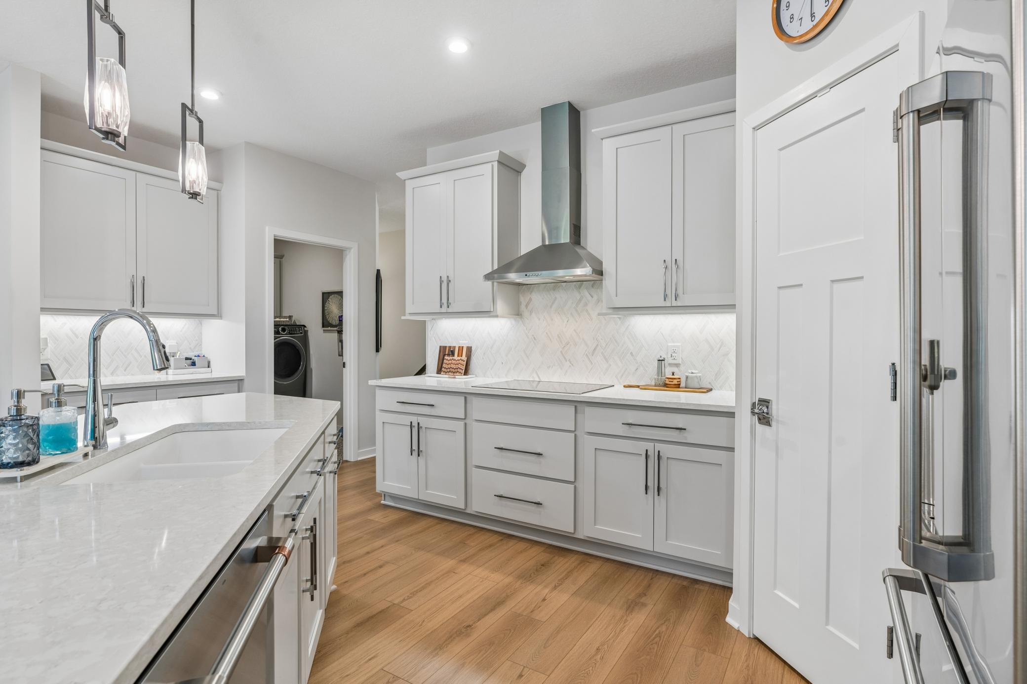 Kitchen with white cabinetry, quartz counters, herringbone backsplash, stainless appliances, and wood flooring