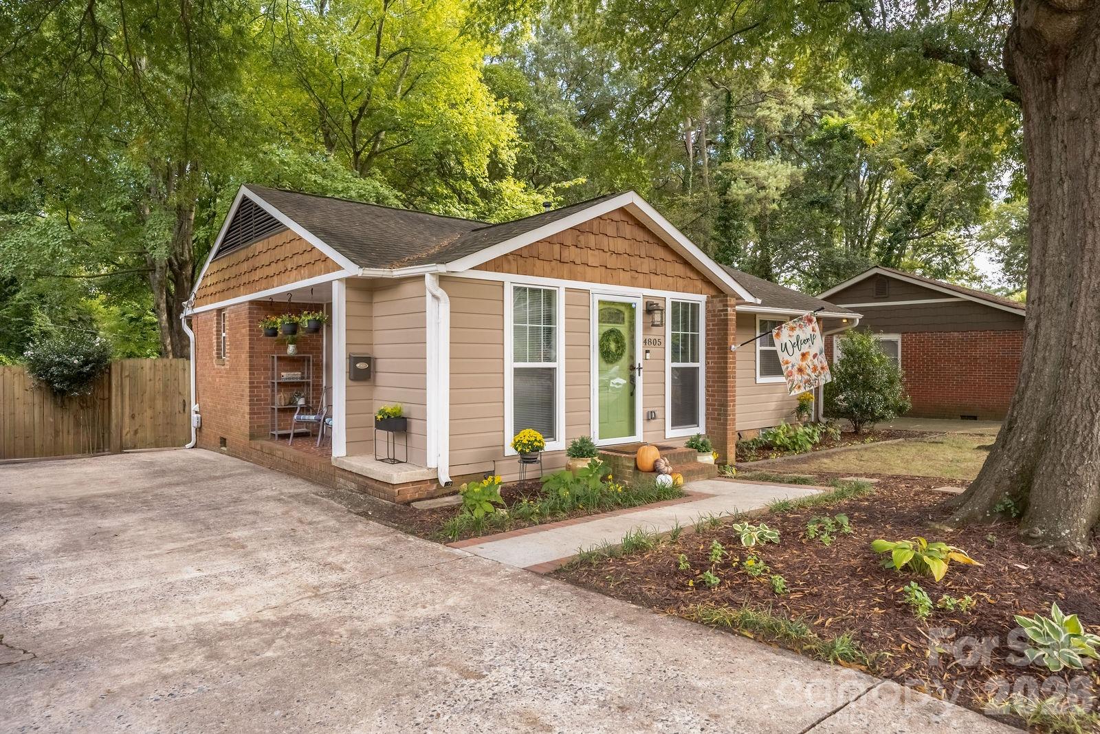 Single-story home with brick accents, a green front door, and a tree-shaded driveway.