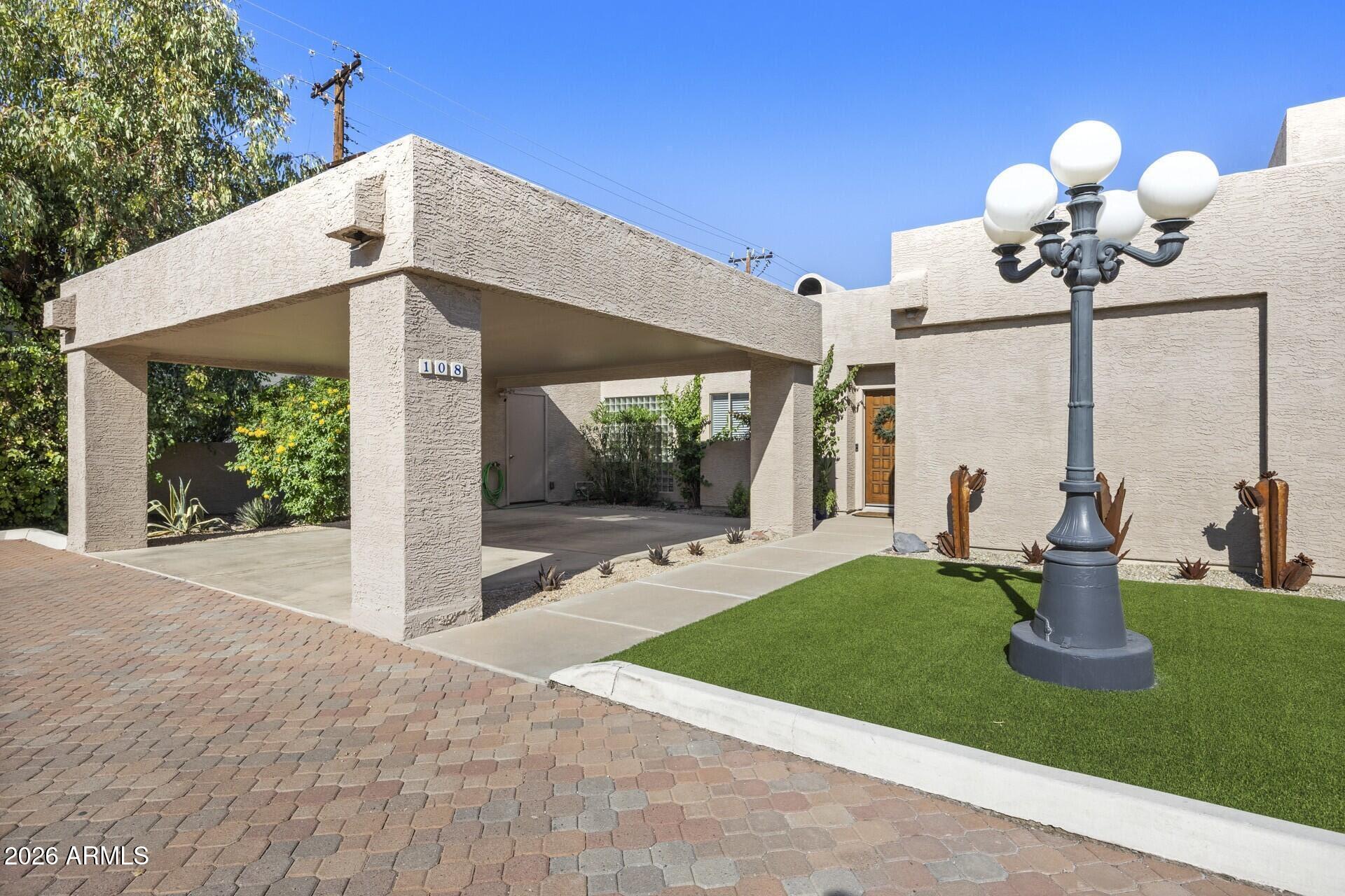 Beige stucco home with a broad covered carport, paved driveway, and turf lawn.
