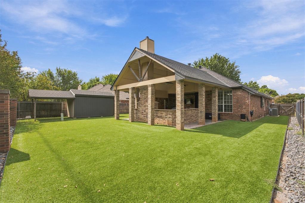 Brick home’s rear exterior with a large covered patio and fenced lawn.
