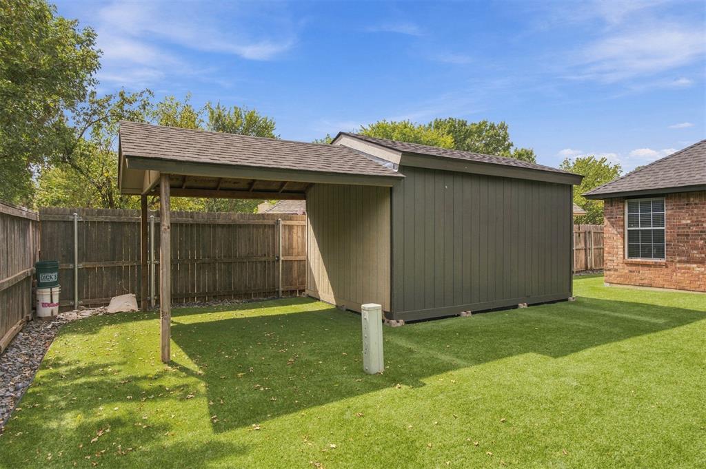 Backyard shed with an attached covered patio beside a fenced lawn.