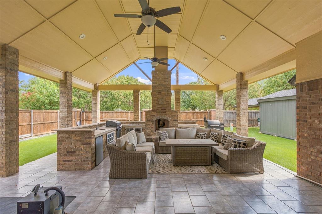Covered patio with wicker seating, a brick fireplace, and an outdoor kitchen.