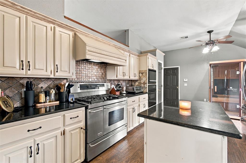 Kitchen with cream cabinetry, stainless steel range, dark counters, and a large island.