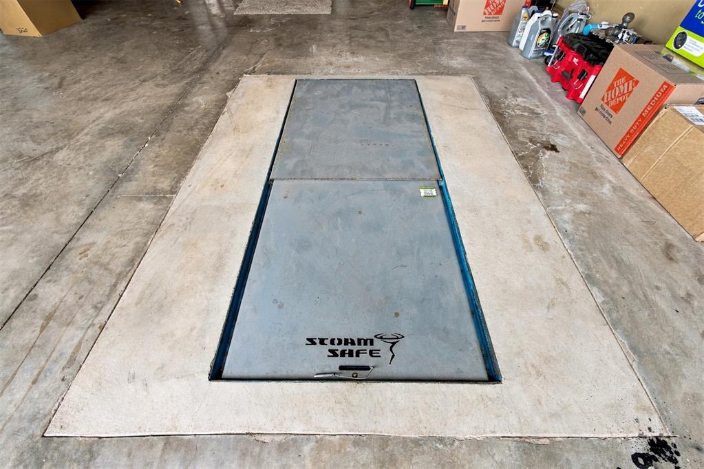 Storm shelter hatch set into the garage floor, with storage boxes and supplies nearby.
